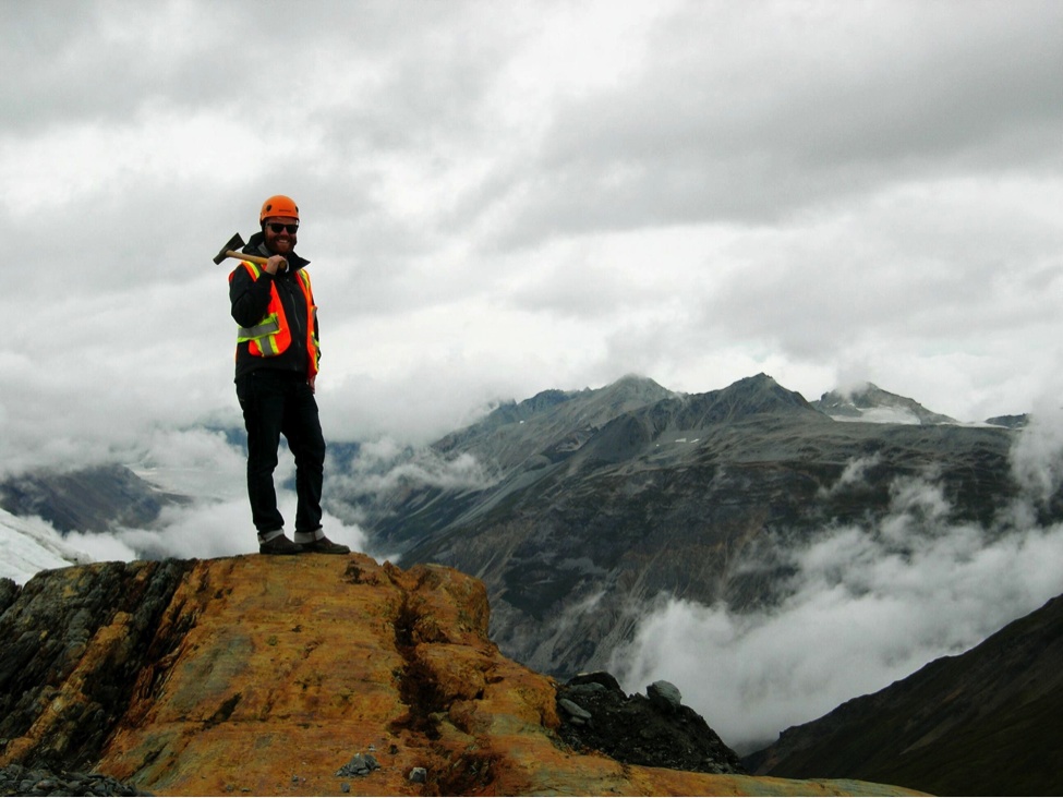 Mining engineer Jamie Keech standing on a precipice overlooking Palmer Project and glacier.